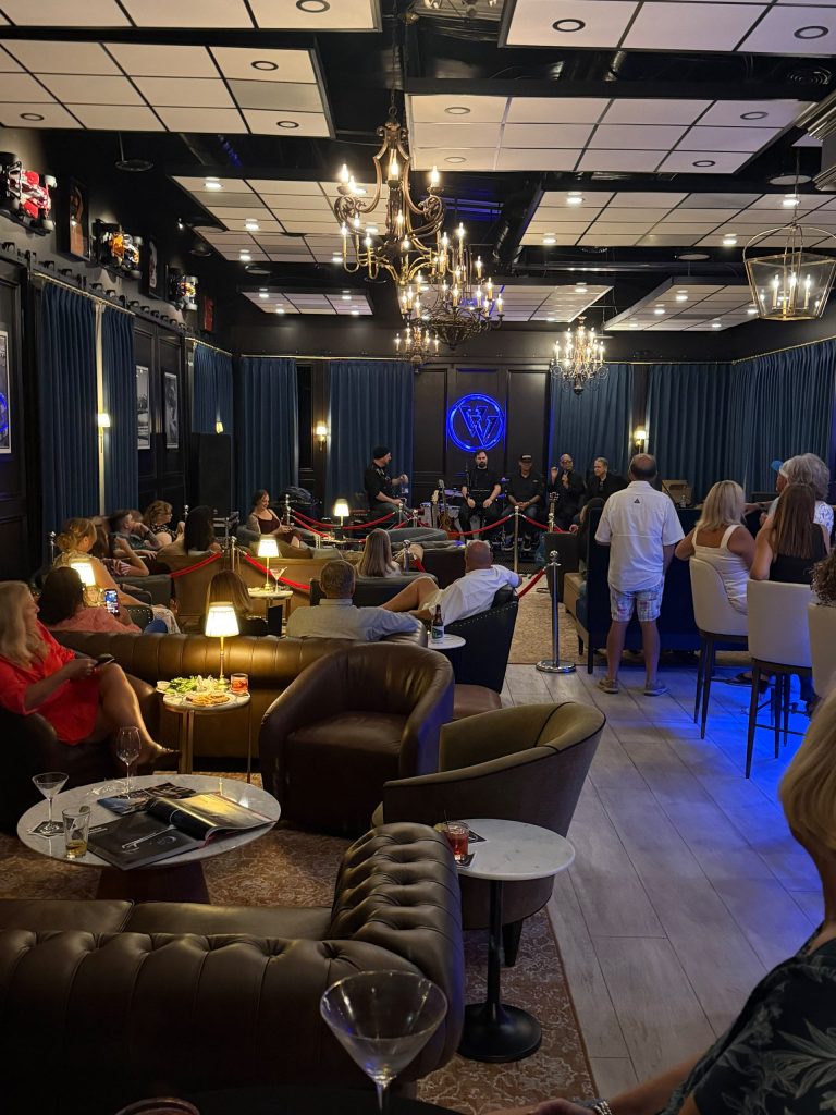 Guests enjoying live entertainment inside the upscale, dimly lit Vehicle Vault social club lounge with leather seating and chandeliers.