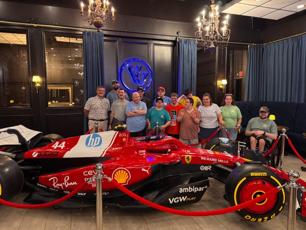 Pockets Full of Sunshine group photo with a red Ferrari Formula 1 show car inside Vehicle Vault Club on Hilton Head Island